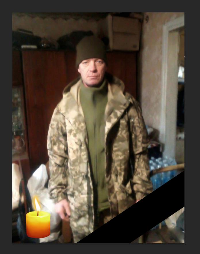 Чоловік у військовому одязі та шапці стоїть у кімнаті.