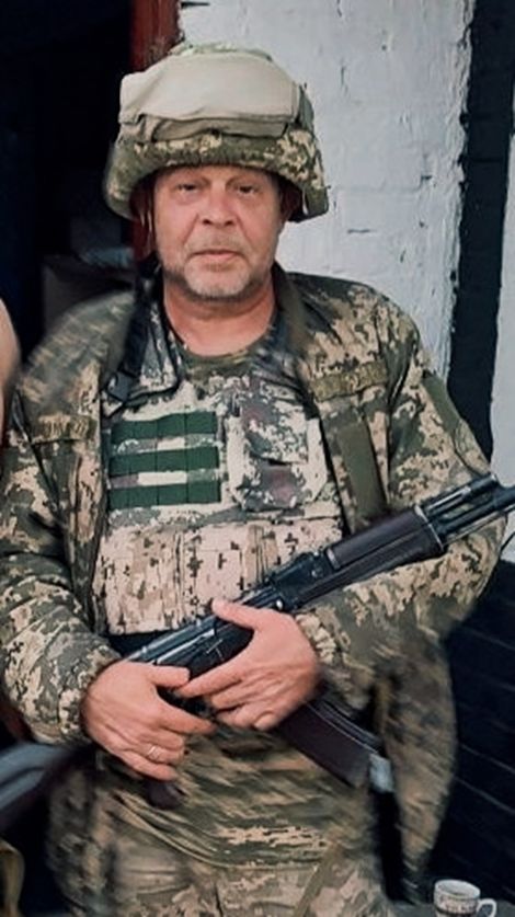 Військовий у камуфляжі та з кулеметом у руках стоїть біля стіни з білою цеглою.