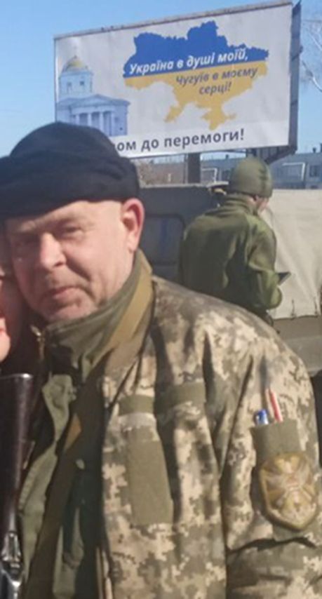 Чоловік у військовій формі дивиться у камеру на тлі білборда із написом українською мовою про любов до України.