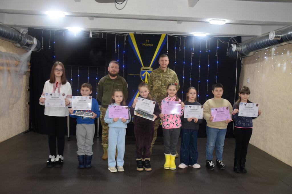 Діти та двоє військових стоять у приміщенні, діти тримають у руках дипломи та відзнаки.