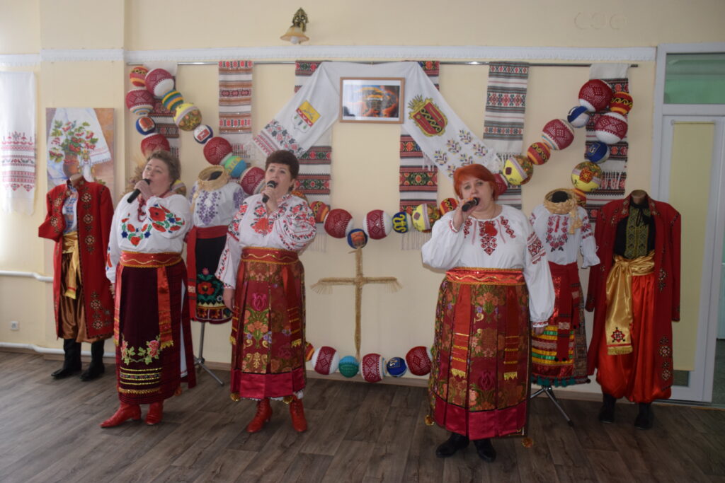 Три жінки у вишиванках співають із мікрофонами в руках.
