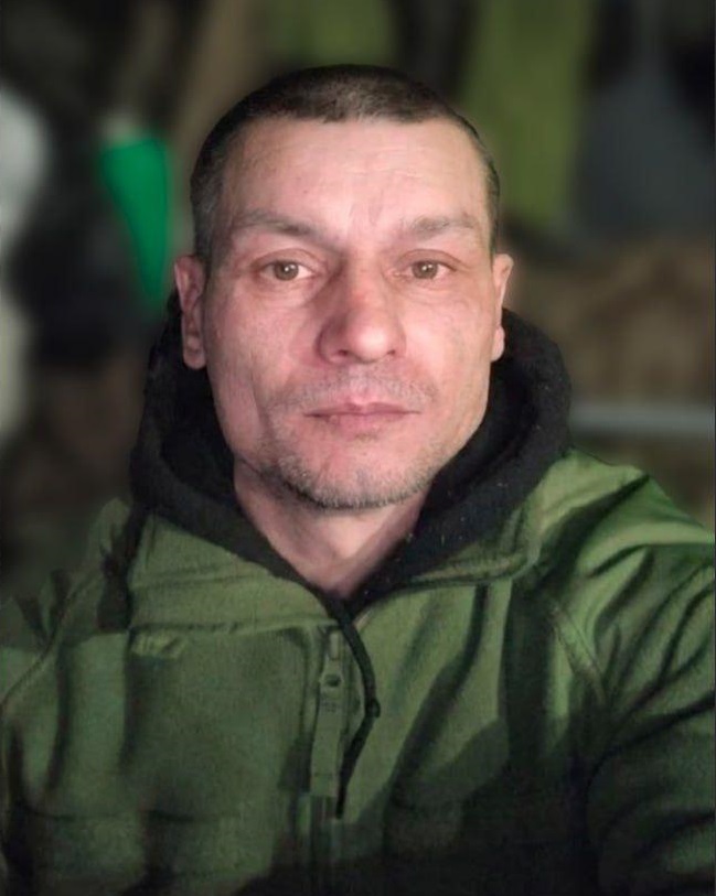Чоловік у зеленій куртці дивиться прямо в камеру.
