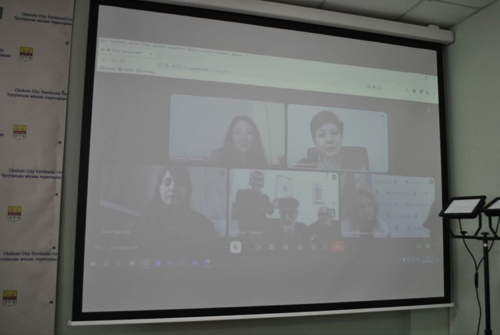 Кілька людей під час відеоконференції на екрані проектора в аудиторії.
