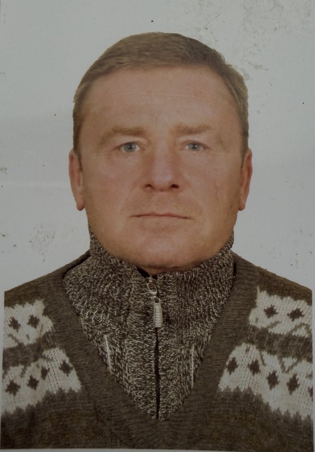 Чоловік зі світло-коричневими волоссями та блакитними очима у в'язаному светрі дивиться прямо в камеру.