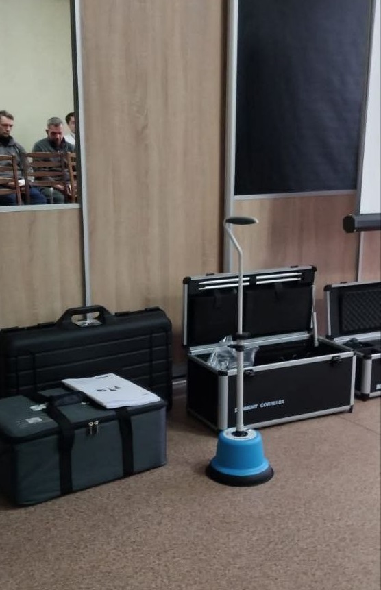 Кілька чорних кейсів із обладнанням розміщено на підлозі аудиторії біля світлої дерев'яної стінки.