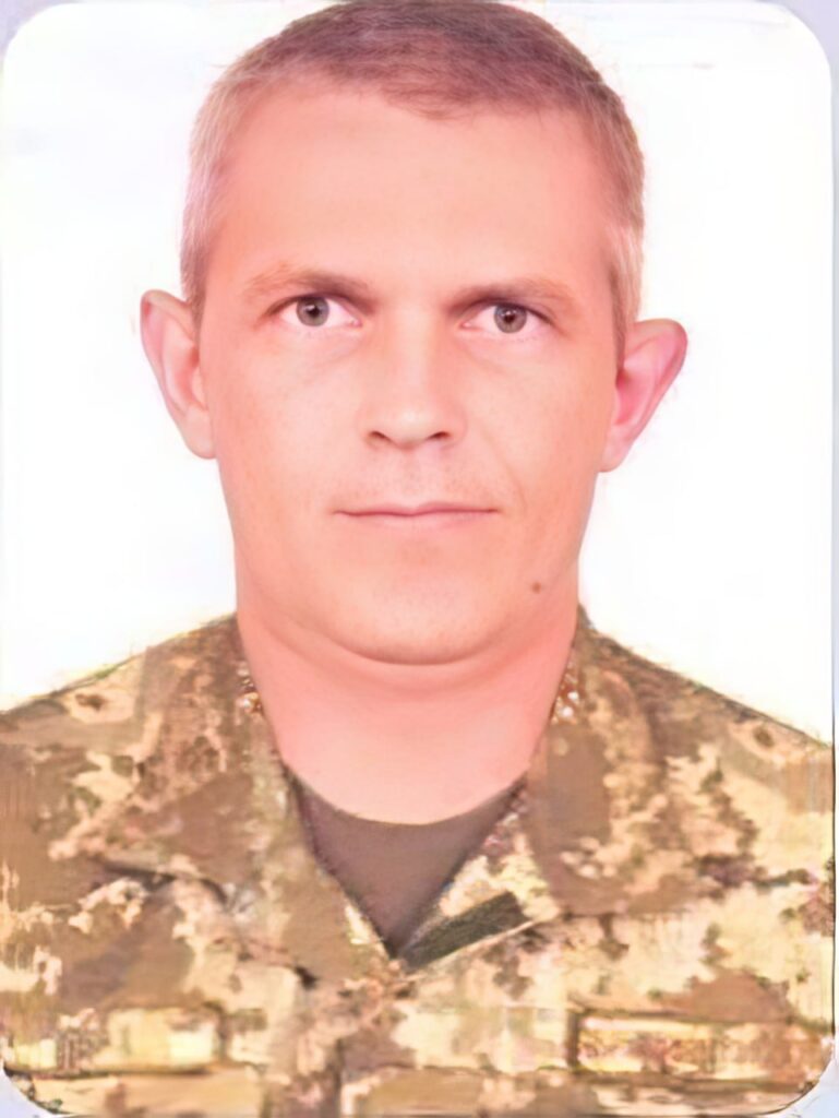 Чоловік у військовій формі дивиться прямо в камеру на білому тлі.