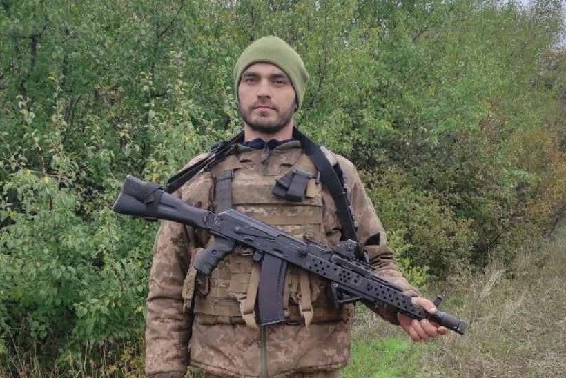 Чоловік у військовій формі та зеленому біреті тримає автомат із приєднаним глушаком.