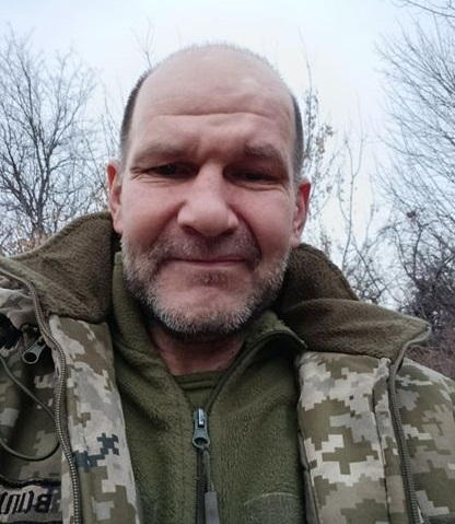 Чоловік у військовій формі та з густою щетиною дивиться у камеру.