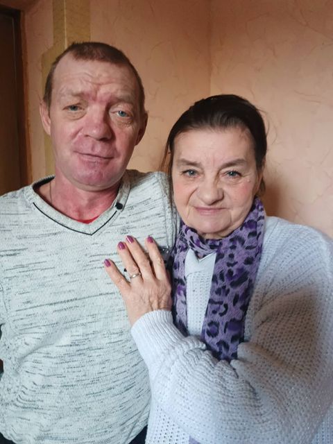 Пара літніх людей, чоловік і жінка, стоять поряд, жінка обіймає чоловіка рукою, на її руці видно обручку.