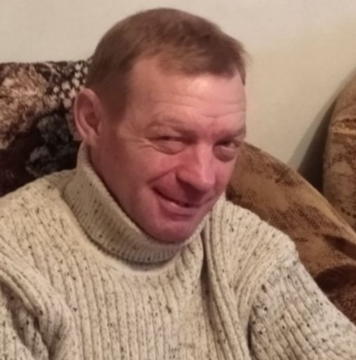 Чоловік із коротким світлим волоссям у світлому светрі дивиться вниз із посмішкою на обличчі.