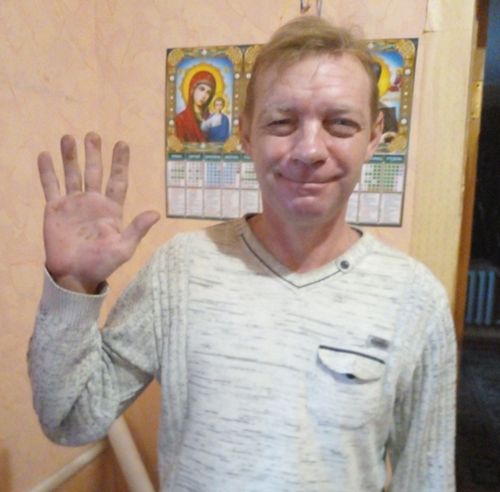 Чоловік зі світло-русявими короткими волоссям підняв долоню правої руки на рівні плеча і дивиться у камеру.