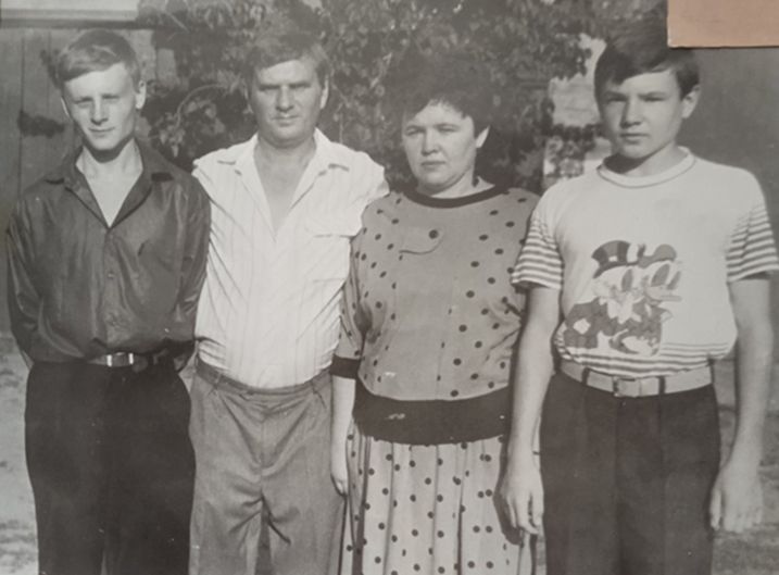 Чорно-біле фото чотирьох людей, які стоять поряд: двоє підлітків у темному та світлому одязі, жінка у сукні в горошок і підліток у світлій футболці з ілюстрацією.