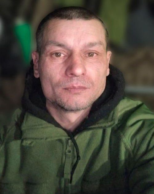Чоловік у зеленому військовому одязі дивиться прямо в камеру.
