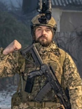 Військовий у камуфляжі підіймає кулак і тримає автомат.