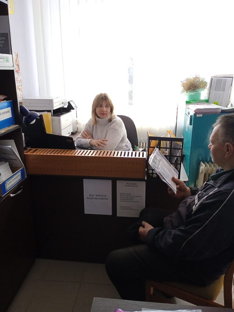 Жінка сидить за столом і дивиться на чоловіка, який сидить навпроти неї та щось читає з паперу.