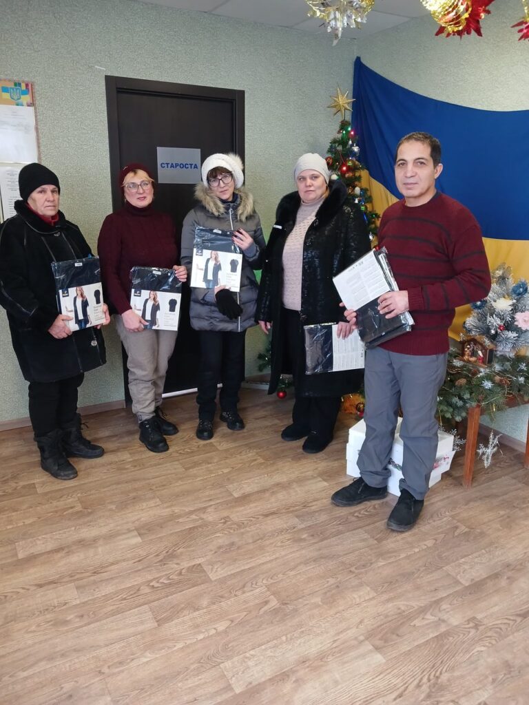 П'ять людей різних вікових груп стоять біля ялинки та тримають у руках пакети й документи.