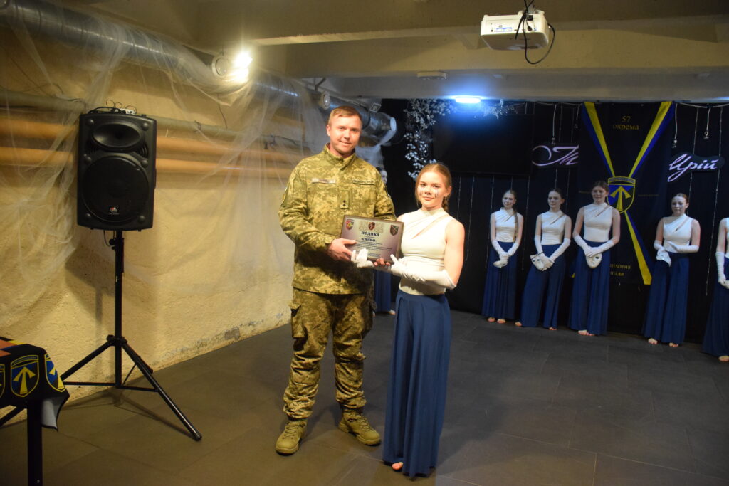 Чоловік у військовій формі вручає жінці в білому топі та синій спідниці нагороду Поділля.