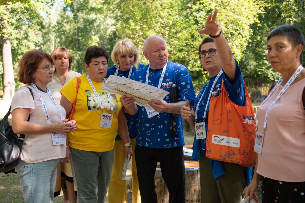 Жінка вказує рукою на щось, показуючи іншим учасникам групи що робити далі згідно з інформаційними матеріалами в руках інших учасників.