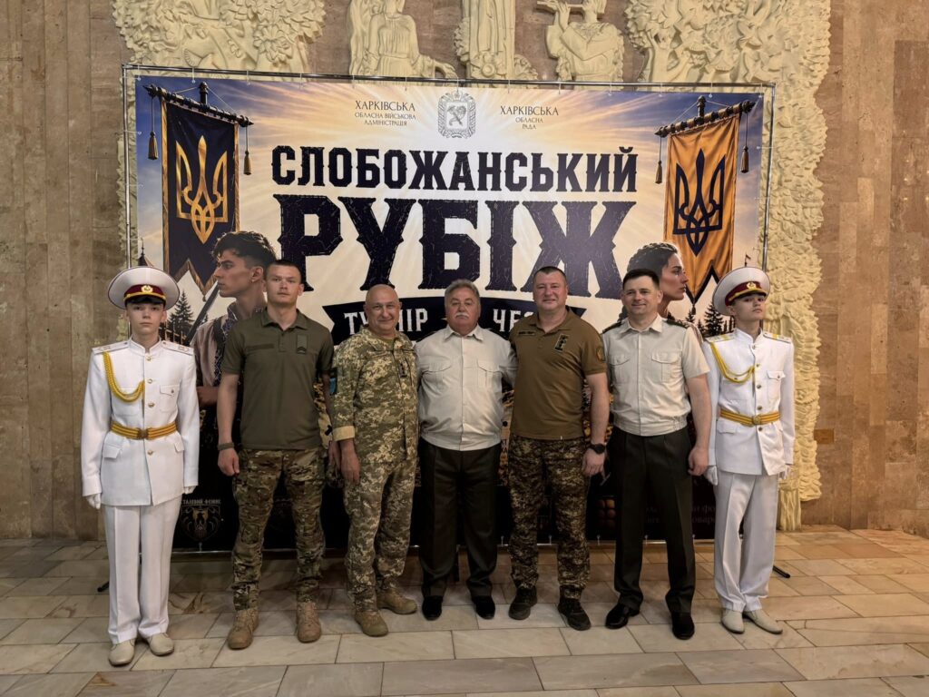 Військові та цивільні особи стоять перед великим банером зі словами «Слобожанський рубіж».