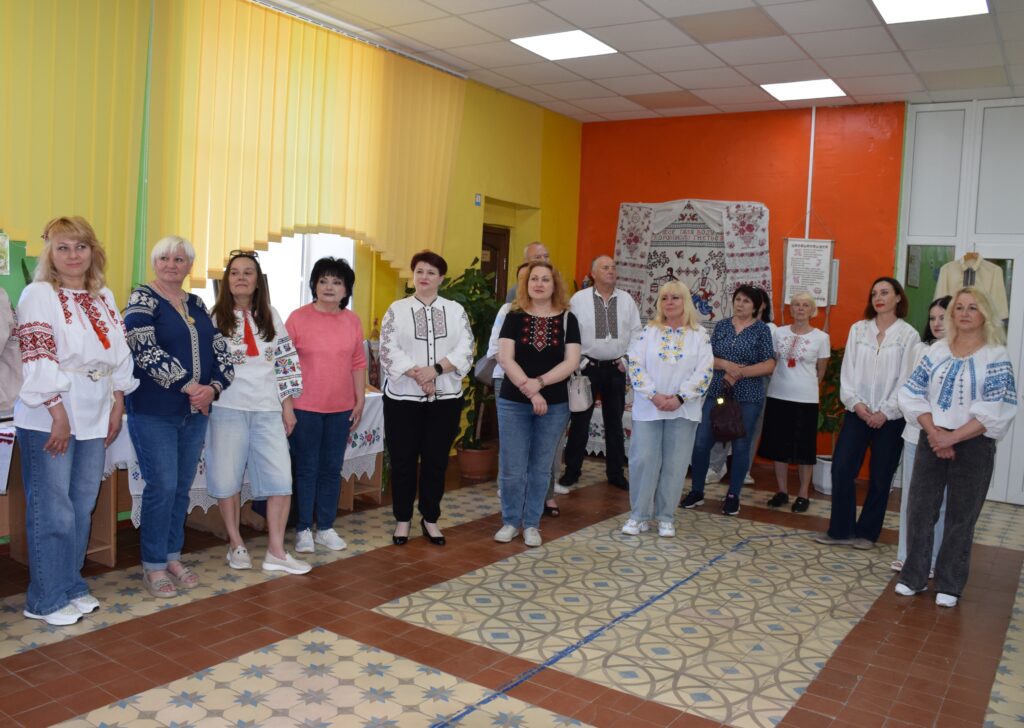 Кілька жінок та чоловіків у вишиванках стоять у приміщенні з кольоровими стінами, утворивши групу людей.