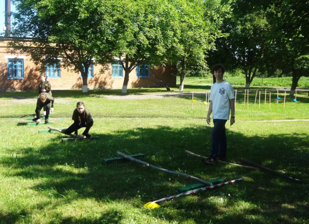 Троє дітей встановлюють перешкоди на газоні біля будівлі.