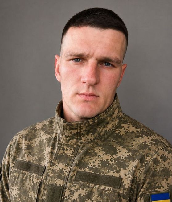Чоловік у військовій формі із українським прапором на рукаві дивиться прямо в камеру.