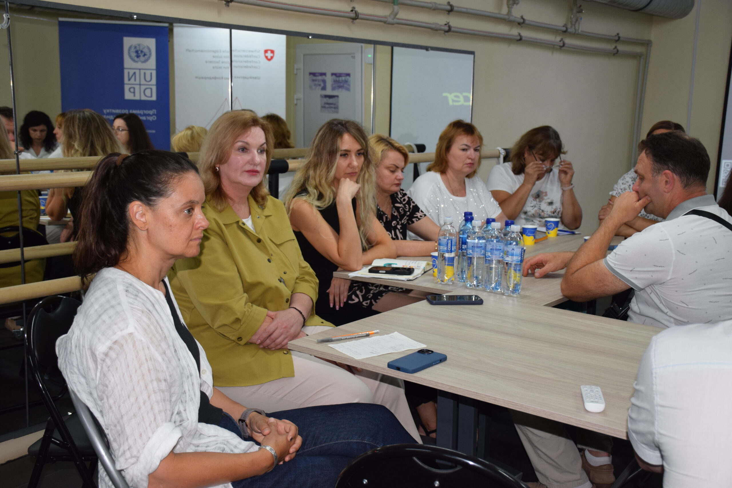 Учасники зустрічі сидять за столом із блокнотами та телефонами на тлі синього банера з логотипом UNDP.