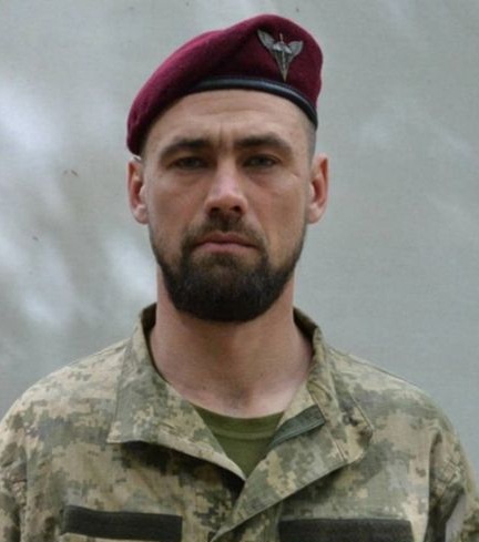 Чоловік у військовій формі та червоному беретi дивиться прямо в камеру.