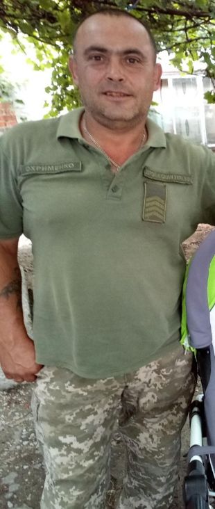 Чоловік у військовій формі та з іменем на шевроні стоїть біля візка.