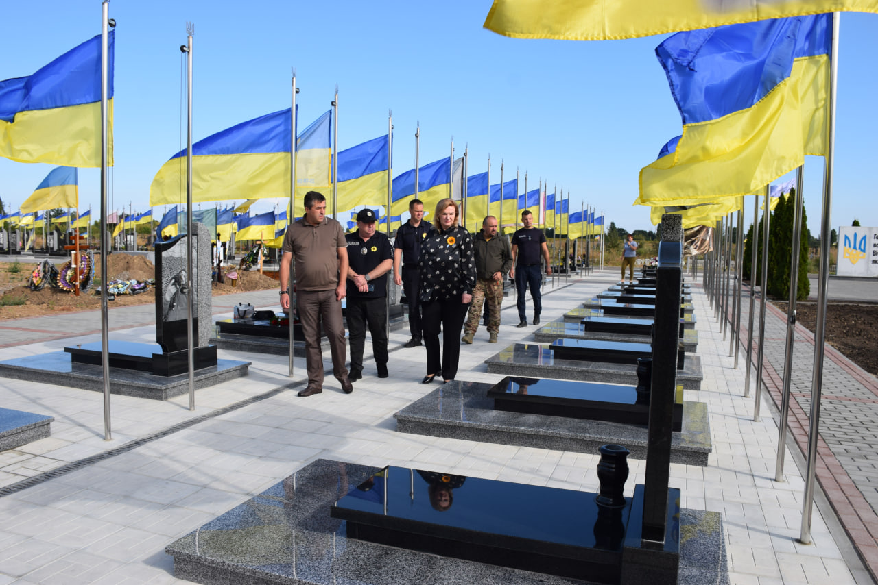 Група людей проходить алеєю між чорними надгробками,