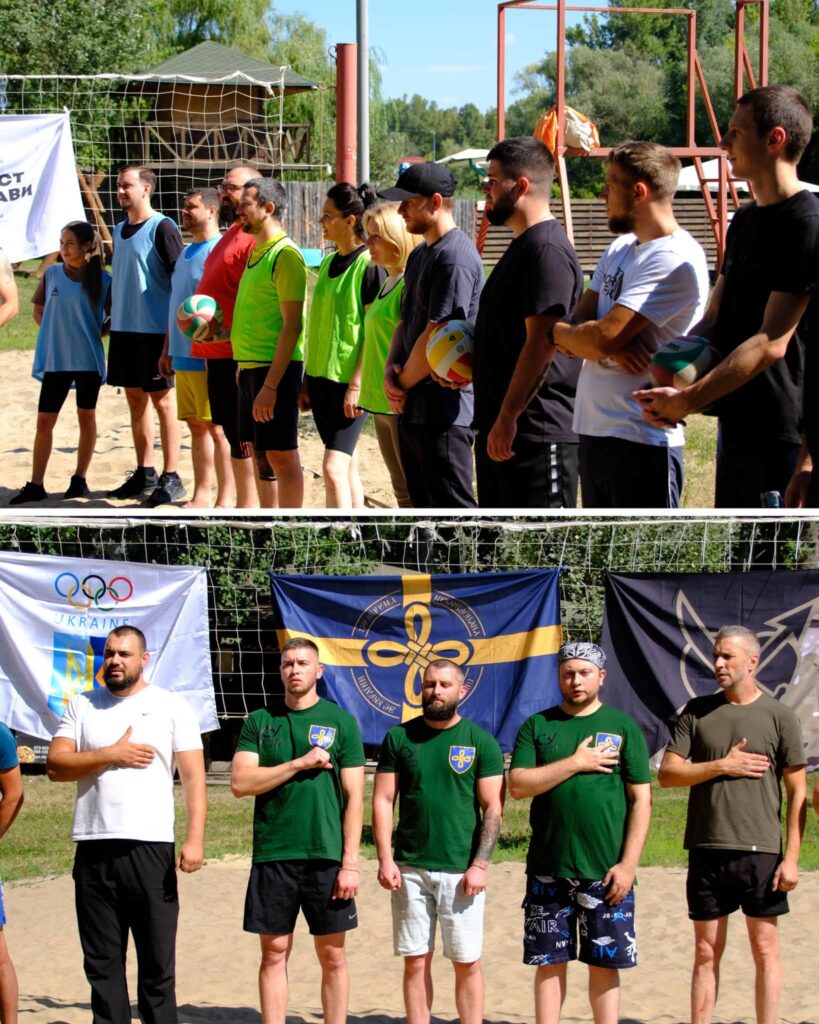 Учасники змагань з пляжного волейболу стоять у шерензі на піску, тримаючи м'ячі або кладучи руки на серце під час урочистої церемонії.