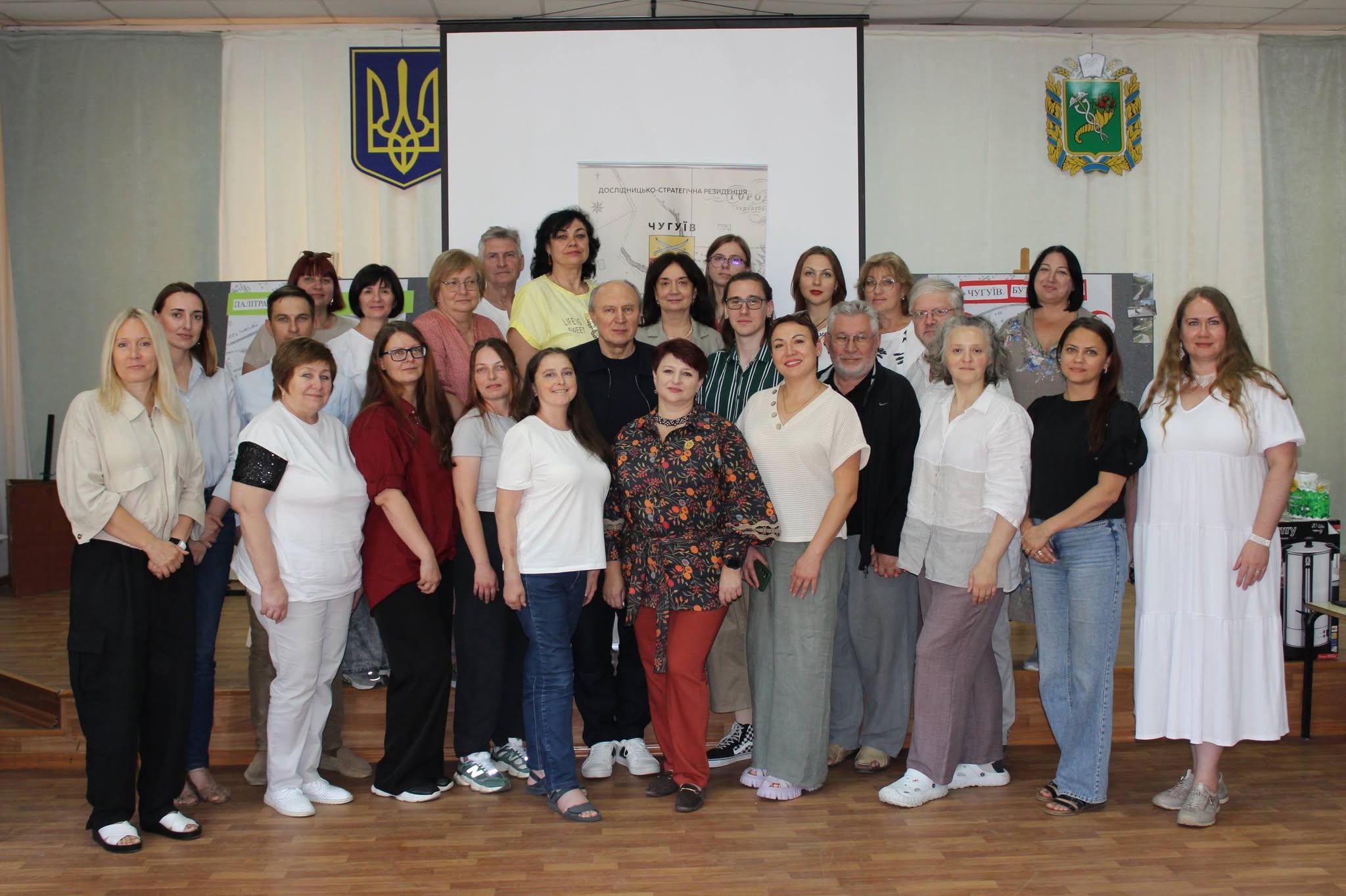 Група людей стоїть у два ряди для спільного фото в залі на тлі українського герба та банера дослідничо-створчої резиденції.