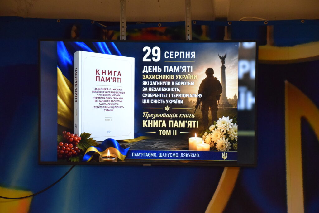На екрані відображається афіша презентації книги «Книга пам'яті. Том II» до Дня пам'яті захисників України 29 серпня, на якій зображено солдата, пам'ятник, свічки та прапор.