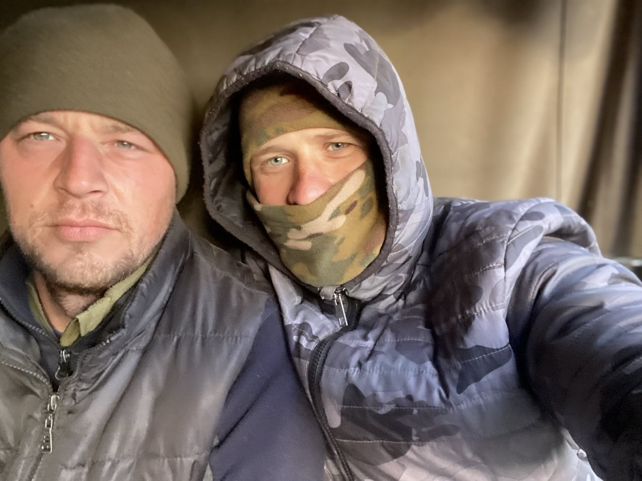 Два чоловіки в зимовому одязі, один у камуфляжі, роблять селфі.