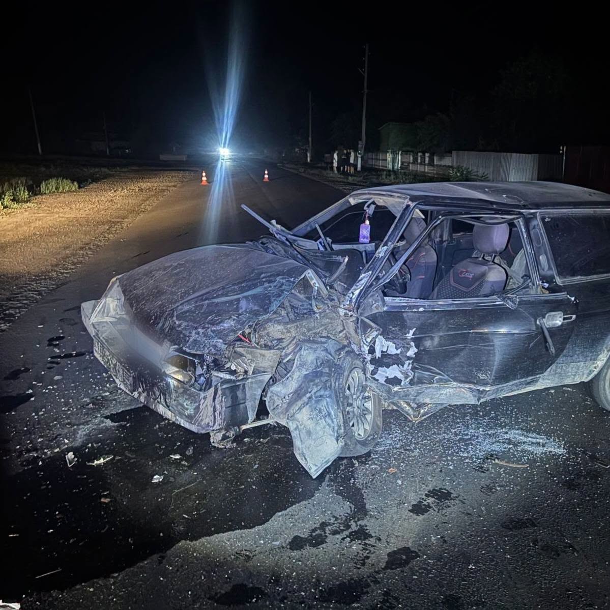 Руйнований автомобіль з розбитим склом та пошкодженим кузовом стоїть на нічній дорозі.