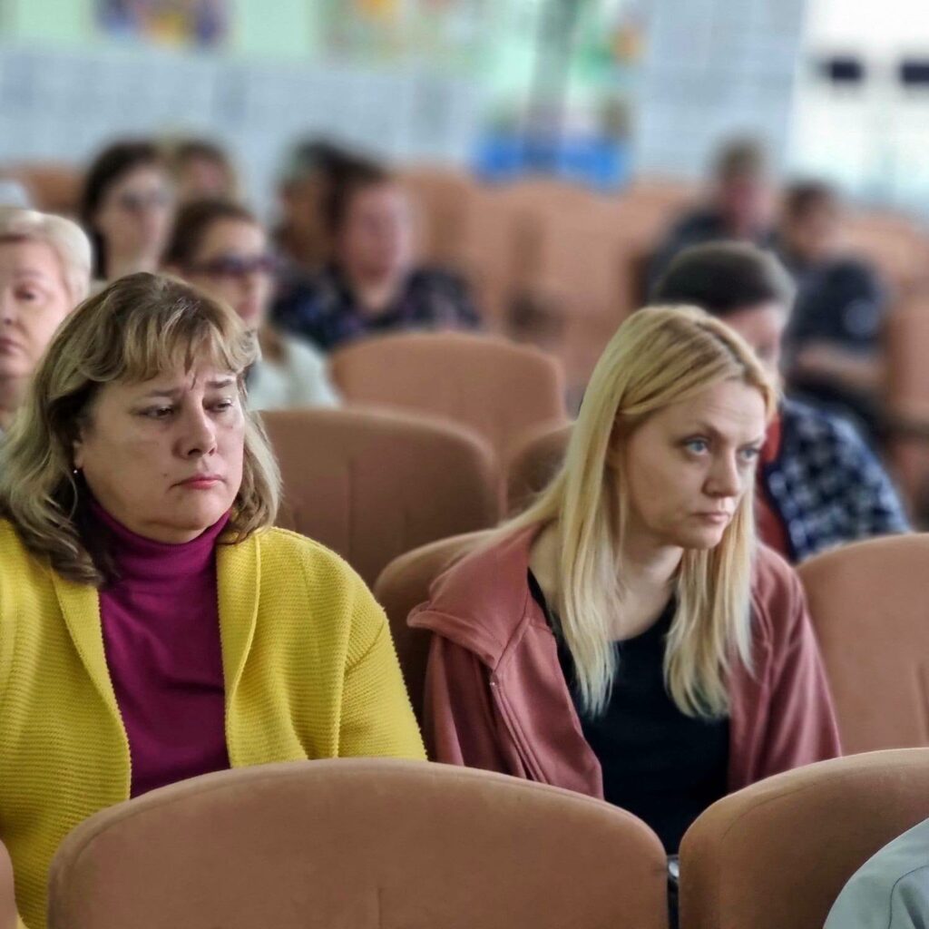 Група людей сидить у залі, зосередивши увагу на чомусь попереду.