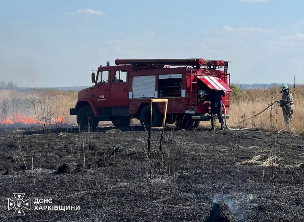 Пожежна машина ДСНС Харківщини та рятувальник гасять трав'яний пожежу на відкритій місцевості.