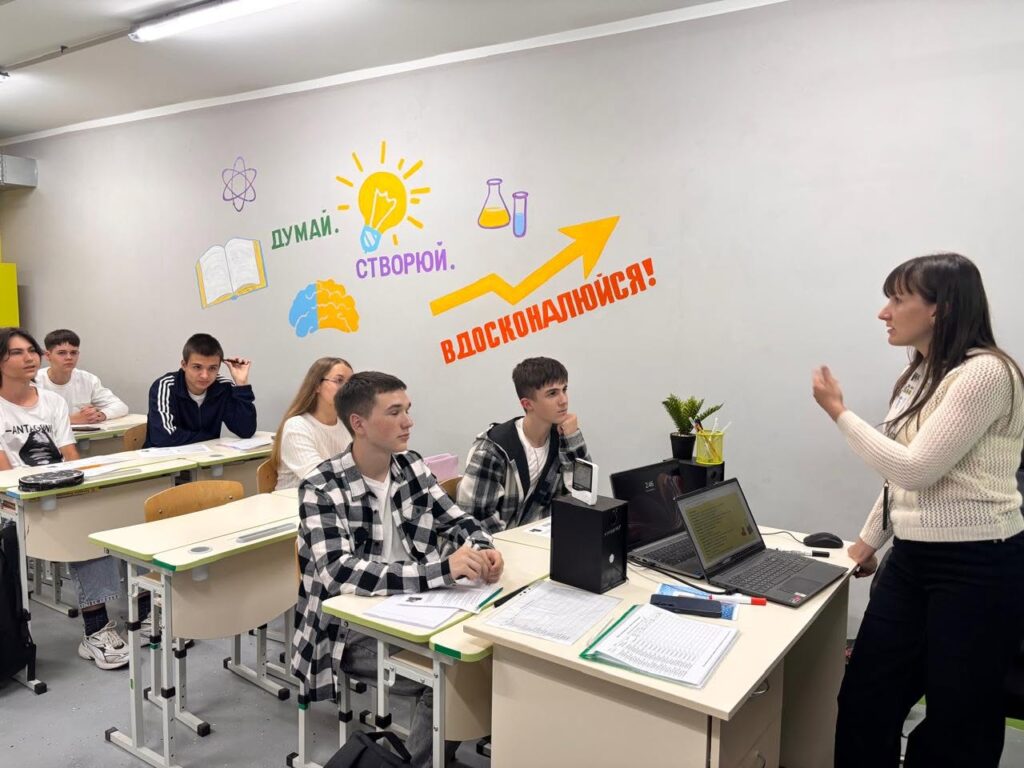 Вчителька проводить урок для учнів у класі, де на стіні написи «Думаю. Створюю. Вдосконалююсь!