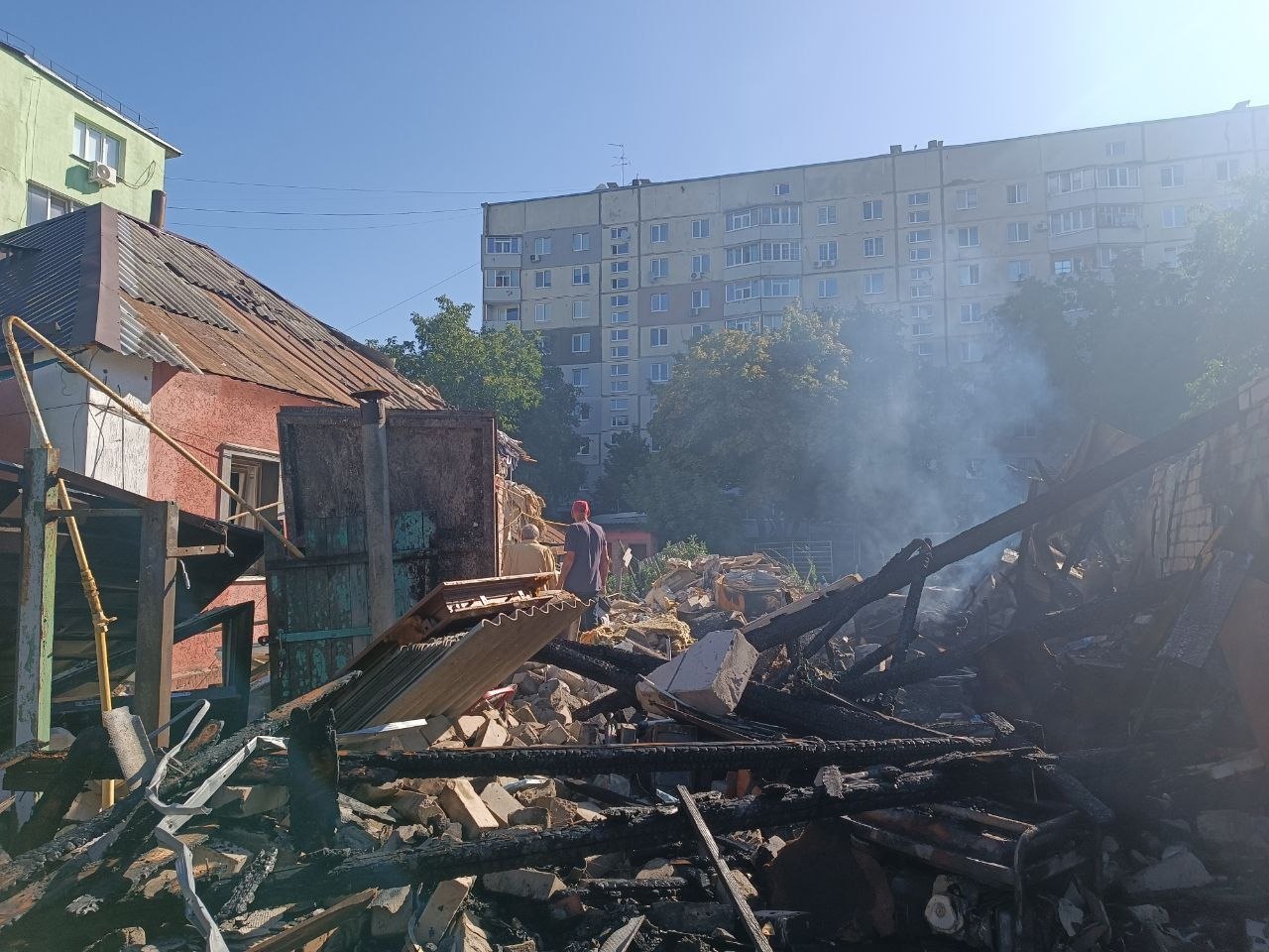 Зруйнована будівля з димом на тлі багатоквартирного житлового будинку.