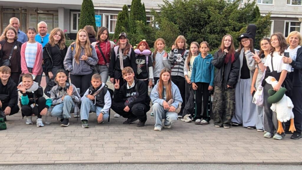 Група дітей та дорослих робить спільне фото на відкритому повітрі, де одна з учасниць тримає велику іграшку качку.