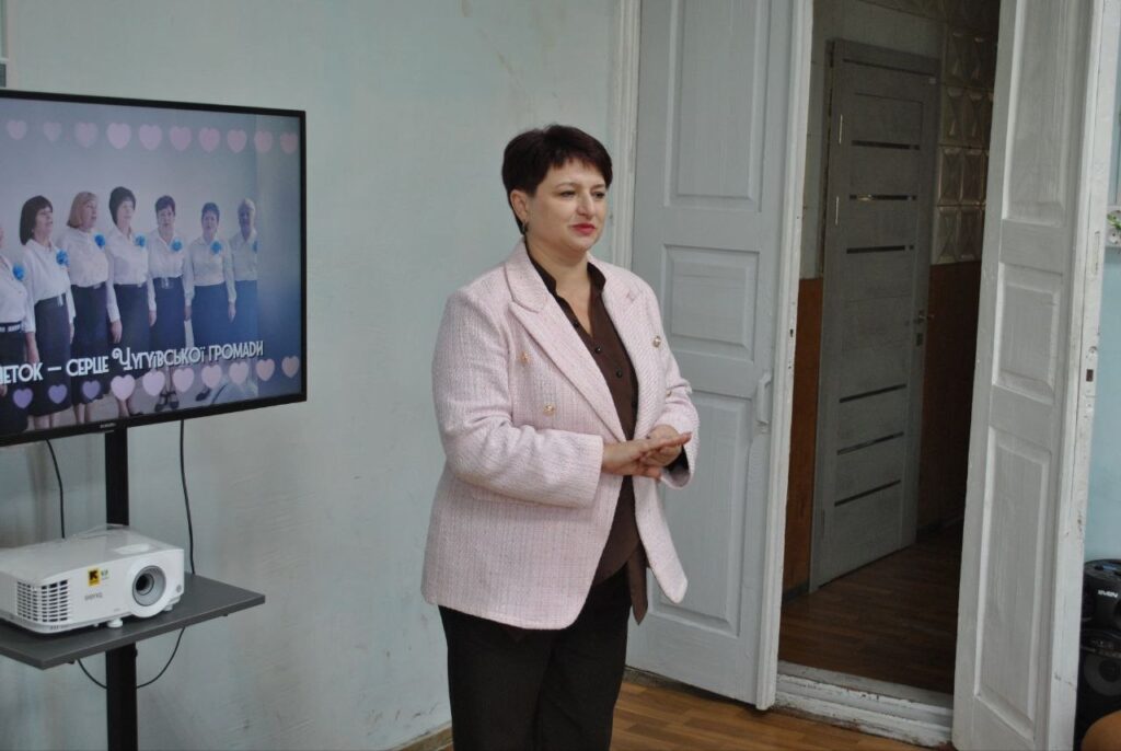 Жінка в рожевому піджаку стоїть біля екрана з написом «Серце Чугуївської громади».