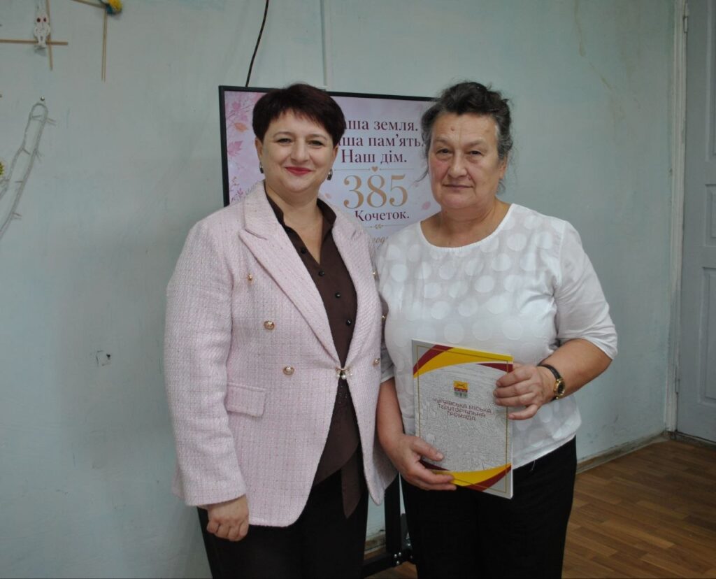 Дві жінки стоять біля банера з написом «Наша земля. Наша пам'ять. Наш дім. 385 Кочеток», одна з них тримає книгу «Історична міська територіальна громада».