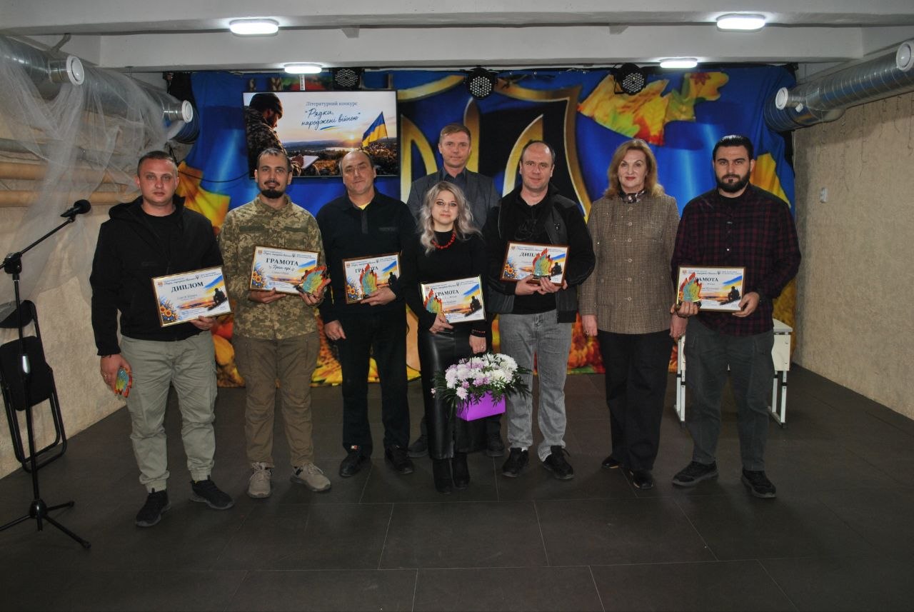 Група людей тримає грамоти та квіти на тлі банера з написом «Радісний вересень».