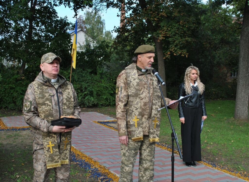 Духовенство в камуфляжі з хрестами на стігарах проводить богослужіння біля українського прапора.