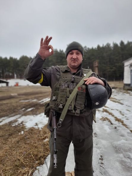 Бойовик у тактичному спорядженні тримає шолом і робить жест 