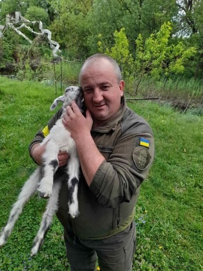 Чоловік в олівійному одязі з нашивкою прапора України тримає на руках білого кролика з чорними плямами.