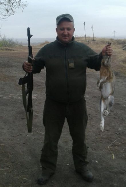 Чоловік у камуфляжі тримає в руках гвинтівку та збитого кролика.