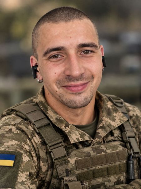 Сміючийся військовослужбовець в камуфляжній формі з українським прапорцем на рукаві