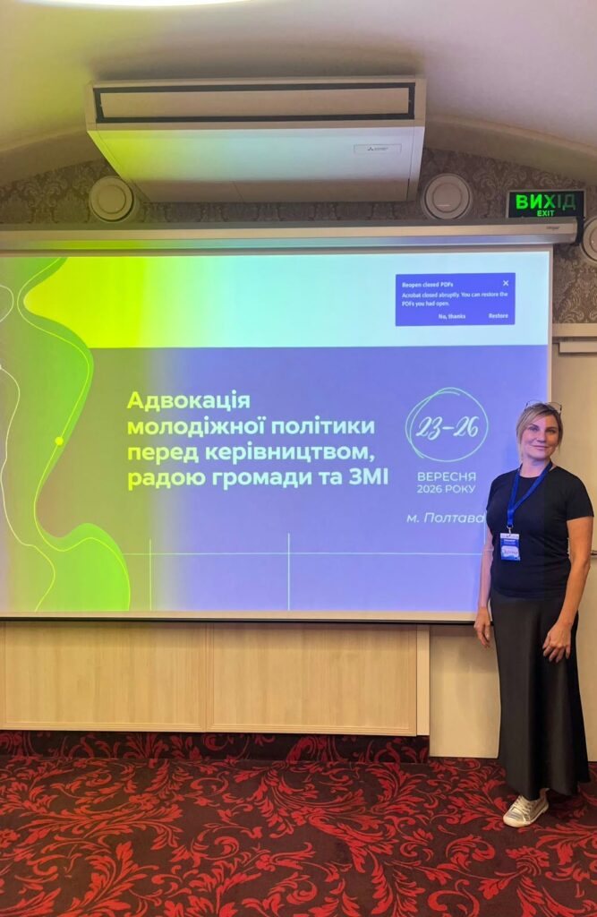 Жінка стоїть біля екрана з презентацією «Адвокація молодіжної політики перед керівництвом, радою громади та ЗМІ».