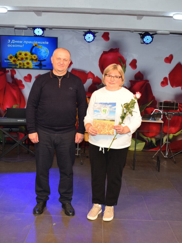 Чоловік і жінка тримають квітку та картину на тлі екрана з написом «З Днем працівників освіти!
